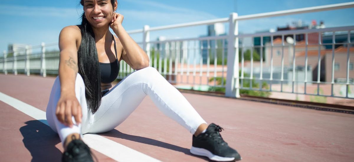 Woman in athletic wear relaxing outdoors on a sunny day, showcasing fitness style and confidence.